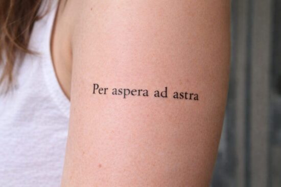 Idee tatuaggi scritte latino: tatuaggio minimal sul braccio con la frase 'Per aspera ad astra' (Attraverso le asperità fino alle stelle).