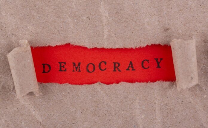 Immagine che rappresenta simbolicamente la crisi di democrazia, con scritta "democracy" al centro.