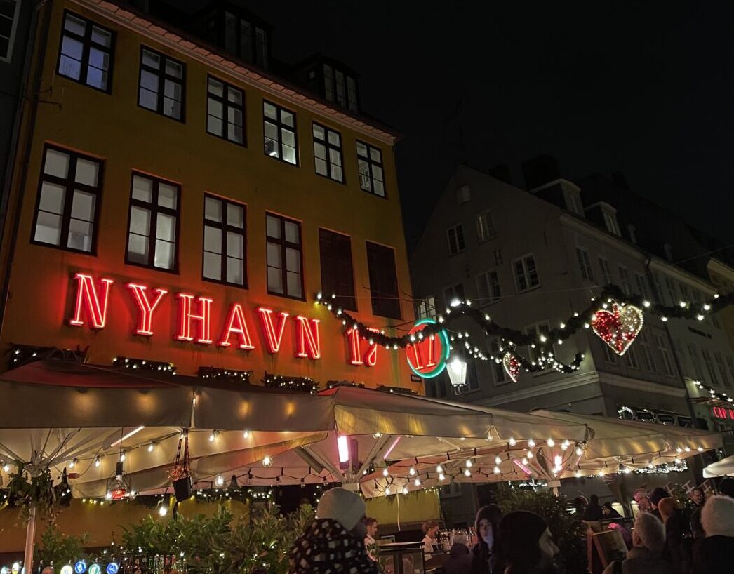 Il canale di Nyhavn a Copenaghen con le case colorate, i bar lungo l’acqua e la scritta “Nyhavn” visibile.